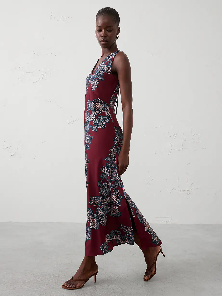Side view of person in a sleeveless maroon floral maxi dress with side slit and heeled sandals.