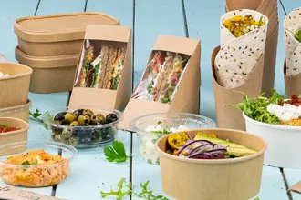 Verschiedene Lebensmittelbehälter, darunter Sandwichdosen, Salatschüsseln und Becher, auf einer hellblauen Oberfläche.