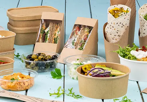 Verschiedene Lebensmittelbehälter, darunter Sandwichdosen, Salatschüsseln und Becher, auf einer hellblauen Oberfläche.
